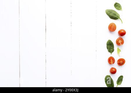 Pose à plat avec des tomates cerises rouges et des feuilles d'épinards vertes sur un fond en bois blanc. Concept d'alimentation saine. Banque D'Images