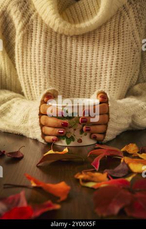 Femme mains tenant le feuillage d'automne et de tasse de thé sur une table sombre Banque D'Images