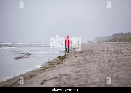 Femme en veste rouge marchant le long de la plage Banque D'Images