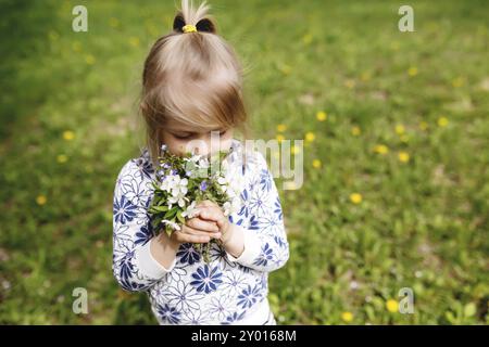 Petite fille reniflant des fleurs de printemps sur la pelouse verte dans le jardin. Banque D'Images