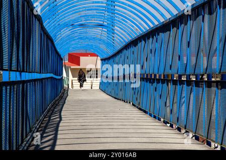 Une femme marchant sur un pont piétonnier. Une femme par derrière au bout d'un pont bleu. Banque D'Images