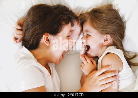 De dessus de la jeune femme heureuse embrassant la petite fille souriante tout en étant allongé sur le lit et en appréciant le temps ensemble Banque D'Images