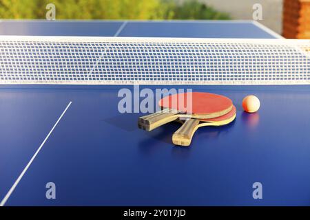 Au-dessus des palettes de ping-pong rouge similaires et petite balle sur la table bleue le jour ensoleillé d'été Banque D'Images