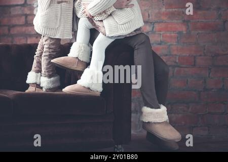 Femme et fille sans visage dans des vêtements chauds et des chaussures assis dans embrasser sur un canapé brun Banque D'Images