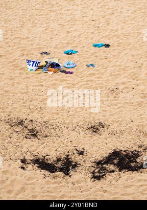 Saint Malo, France - 20 juillet 2024 : plage de sable avec serviette colorée, sac fourre-tout, vêtements et débris d'algues. Banque D'Images