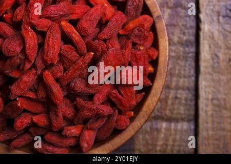 Baies de Goji dans un bol en bois sur une vieille planche rustique, mise au point sélective, macro Banque D'Images