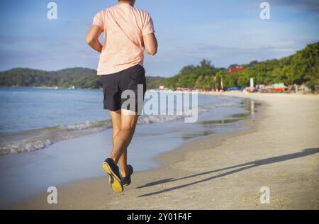 Jeune homme qui court sur la plage au lever du soleil Banque D'Images