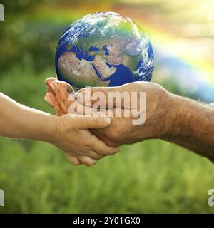 Homme senior et bébé tenant la Terre dans les mains contre un arc-en-ciel au printemps. Concept d'écologie Banque D'Images