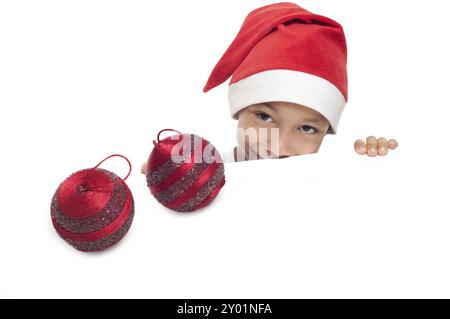 Garçon curieux dans le chapeau rouge avec deux boules décoratives de noël isolées sur fond blanc avec un espace de copie vide pour placer la publicité ou la bannière Banque D'Images