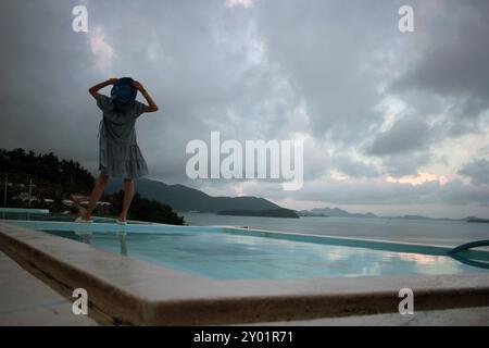 Dolsan-eup, Yeosu-si, Corée du Sud - 26 juillet 2024 : jeune femme regardant le lever du soleil dans un complexe avec piscine donnant sur la mer à Yeosu Banque D'Images