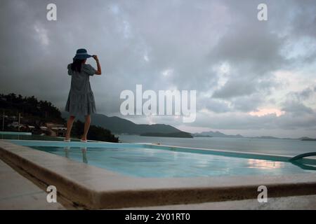 Dolsan-eup, Yeosu-si, Corée du Sud - 26 juillet 2024 : jeune femme regardant le lever du soleil dans un complexe avec piscine donnant sur la mer à Yeosu Banque D'Images