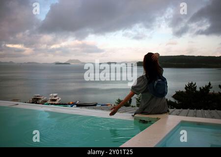 Dolsan-eup, Yeosu-si, Corée du Sud - 26 juillet 2024 : jeune femme regardant le lever du soleil dans un complexe avec piscine donnant sur la mer à Yeosu Banque D'Images