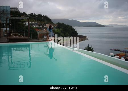 Dolsan-eup, Yeosu-si, Corée du Sud - 26 juillet 2024 : jeune femme regardant le lever du soleil dans un complexe avec piscine donnant sur la mer à Yeosu Banque D'Images