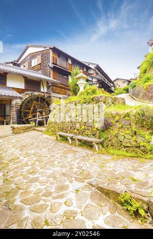 Des maisons traditionnelles en bois et une roue à eau bordent le chemin de pierre sur cette section magnifiquement restaurée de la route historique Nakasendo de l'époque d'Edo en gare Banque D'Images