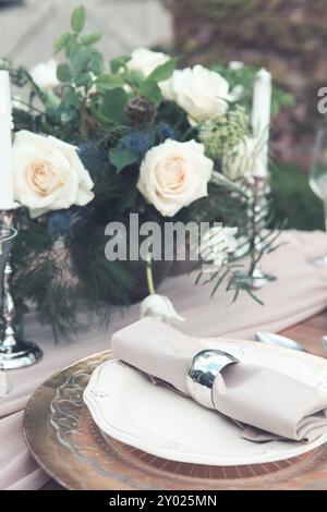 Bougies et vase avec des roses blanches placées sur la table ronde près des verres à vin pendant la date romantique dans le jardin Banque D'Images