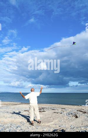 Un homme âgé vole un cerf-volant sur une plage en face d'une mer calme et d'un paysage nuageux spectaculaire d'été. Un homme vole un cerf-volant sur une plage en face d'une mer calme et Banque D'Images