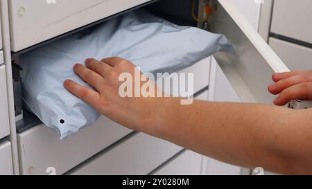 Une personne vient chercher un colis dans un terminal de colis. La main tient les marchandises emballées pour l'envoi par une boîte aux lettres. Banque D'Images