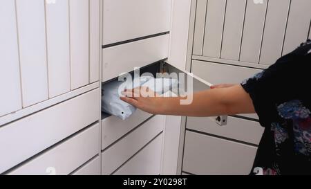 Une fille reçoit un colis d'une machine à colis. Les mains des femmes sortent un colis emballé d'une boîte aux lettres. Banque D'Images