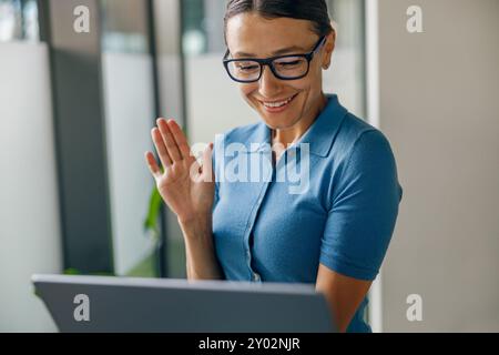 Une femme professionnelle participe activement à un appel vidéo avec son ordinateur portable présent devant elle Banque D'Images