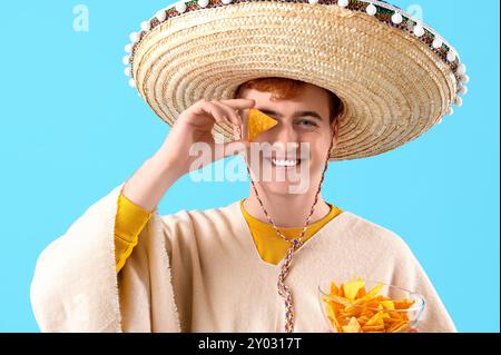 Portrait de jeune homme mexicain en sombrero et avec nachos sur fond bleu Banque D'Images