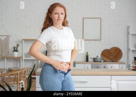 Une jeune femme bouleversée en jeans serrés à la maison. Concept de gain de poids Banque D'Images