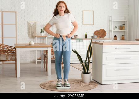 Bouleversé jeune femme en jeans serrés sur des balances à la maison. Concept de gain de poids Banque D'Images