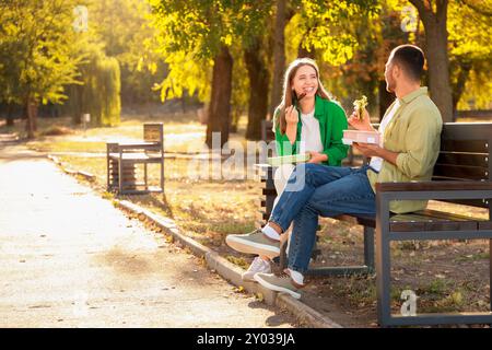 Jeune couple déjeunant sur le banc dans le parc Banque D'Images