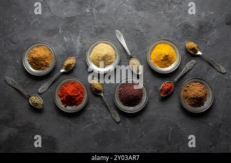 Assortiment d'épices naturelles sur des cuillères en argent vintage ou des plats sur fond de pierre rustique foncé, concept d'épices saines Banque D'Images