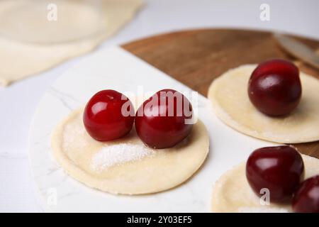 Procédé de fabrication de boulettes (varenyky) avec des cerises. Pâte crue et ingrédients sur table blanche, gros plan Banque D'Images