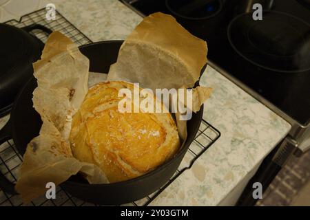 Vue de dessus d'un pain noir hollandais à croûte dorée avec du papier parchemin, assis sur le comptoir marbré refroidissant sur la grille du four avec le papier brûlé Banque D'Images