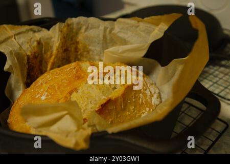 Vue de dessus d'un pain noir hollandais à croûte dorée avec du papier parchemin, assis sur le comptoir marbré refroidissant sur la grille du four avec le papier brûlé Banque D'Images