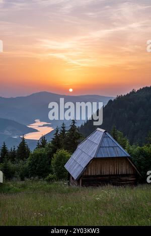 Belle vue sur la petite cabane en bois et le lac Zaovine pendant le coucher du soleil au point de vue Zmajevac, montagne Tara, Serbie. Banque D'Images