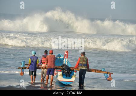 Purworejo, Java central, Indonésie. 30 août 2024. De petits bateaux transportant deux à trois pêcheurs ont bravé de hautes vagues par mauvais temps pour aller pêcher à la plage de Jatimalang sur AÄŸust, 30, 2024. Le mauvais temps et les vents violents n’ont pas découragé les pêcheurs de partir en mer. Ils ont utilisé leur instinct et leurs connaissances pour braver les vagues de huit mètres de haut pour se rendre au milieu de la mer, seuls quelques bateaux de pêche ont osé commencer à pêcher dès l’aube et revenir à midi parce qu’ils ne voulaient pas prendre trop de risques pendant la mauvaise saison météo. (Crédit image : © Dasril Roszandi/ZUMA Press Wire) EDITORIAL Banque D'Images