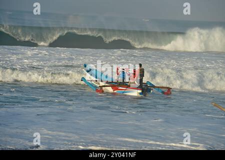 Purworejo, Java central, Indonésie. 30 août 2024. De petits bateaux transportant deux à trois pêcheurs ont bravé de hautes vagues par mauvais temps pour aller pêcher à la plage de Jatimalang sur AÄŸust, 30, 2024. Le mauvais temps et les vents violents n’ont pas découragé les pêcheurs de partir en mer. Ils ont utilisé leur instinct et leurs connaissances pour braver les vagues de huit mètres de haut pour se rendre au milieu de la mer, seuls quelques bateaux de pêche ont osé commencer à pêcher dès l’aube et revenir à midi parce qu’ils ne voulaient pas prendre trop de risques pendant la mauvaise saison météo. (Crédit image : © Dasril Roszandi/ZUMA Press Wire) EDITORIAL Banque D'Images