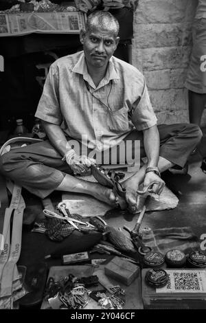 Homme de réparation de chaussures de cordonnier indien local dans une rue de Mumbai Inde. Cordonnier indien travaillant sur la réparation de chaussures dans son atelier. Photo de voyage, vue sur la rue, éditeur Banque D'Images