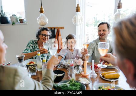 Joyeuse famille multigénérationnelle griller des boissons tout en étant assis à table pour dîner à la maison Banque D'Images