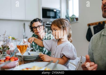 Fille mangeant le dîner tout en étant assis à la table à manger avec la famille à la maison Banque D'Images