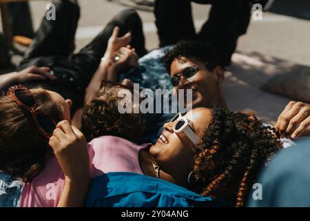 Heureuse jeune femme à la mode couchée sur le sol avec des amis masculins et féminins au soleil Banque D'Images