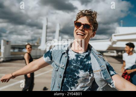Portrait de jeune homme joyeux dans des lunettes de soleil avec bras tatoué appréciant avec des amis dans le parking Banque D'Images