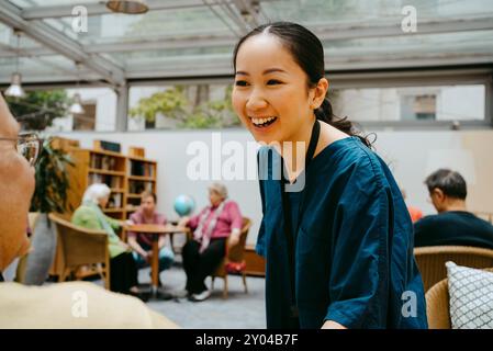 Heureuse jeune femme soignante parlant avec un homme âgé en maison de retraite Banque D'Images