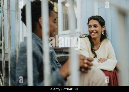 Adolescente heureuse parlant avec un cousin mâle et assise sur des marches à l'extérieur de la maison Banque D'Images