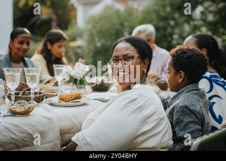 Portrait de femme âgée heureuse avec des lunettes regardant par-dessus l'épaule tout en étant assis avec les membres de la famille au déjeuner Banque D'Images