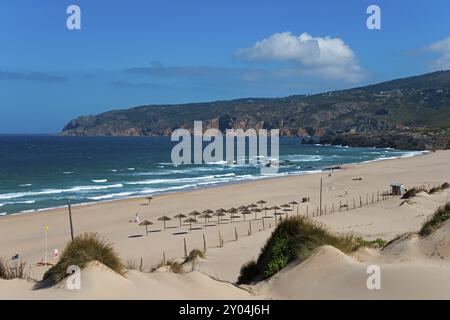 Plage avec des dunes de sable et des parasols, derrière eux la mer et les rochers, ciel partiellement nuageux, dune en mouvement, Duna da Cresmina, système de dunes Guincho-Cresmina, du Banque D'Images