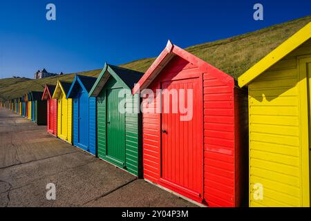Les cabanes de plage en bois colorées de Whitby bordent la promenade. Le matin, ils attrapent le soleil tôt. Banque D'Images