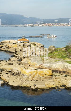 Rias Baixas Seascape avec phare Punta Cabalo et bateau à moules naviguant entre les lits de moules appelés bateas. Galice, Espagne, Europe Banque D'Images