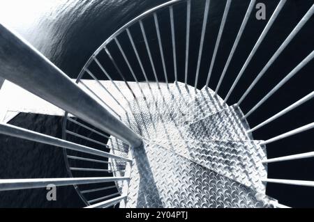 Vue en descendant un escalier en colimaçon en métal tournant autour d'un poteau central alors qu'il serpente vers le bas, image monochrome et fleurs d'acier froides. VI Banque D'Images