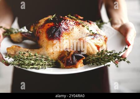 Crochez la femelle en robe noire tenant la plaque blanche avec un poulet grillé appétissant et croustillant aux fruits et au thym vert Banque D'Images