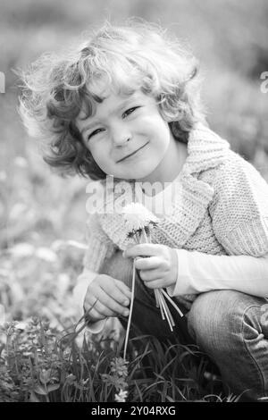 Enfant souriant tenant un bouquet de fleurs. Photo noir et blanc Banque D'Images