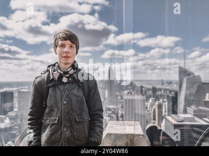 Jeune homme adulte aux cheveux bruns et à la barbe regardant la caméra tout en se tenant sur une tour d'observation devant la ville de New york, états-unis, amérique Banque D'Images