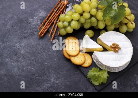 Planche d'ardoise avec brie au fromage, raisins blancs, craquelins noix et vin sur pierre noire, vue horizontale de dessus Banque D'Images